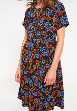 Kwiatowa sukienka z krótkimi rękawami, z niebieskimi i pomarańczowymi kwiatami na granatowym tle, zebrana w talii i z dekoltem w kształcie łezki.