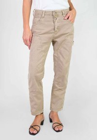 Beige cargobroek met meerdere zakken, textuurstof, rechte pijp pasvorm en een knoopsluiting. Gecombineerd met zwarte sandalen met bandjes.