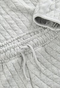 Harmaa tikkikangas, jossa on herringbone-kuvio. Varustettu kiristysnauhalla ja ribbitatuilla hihoilla. Pehmeä tekstuuri ja kodikas ilme.