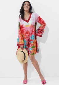 Bunt gekleidetes Kleid mit einem lebhaften Palmenmuster in Rot, Pink und Türkis, mit Glockenärmeln und einem V-Ausschnitt. Mit einem blumigen Rand akzentuiert.