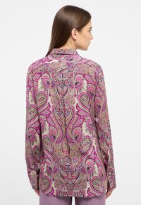 Long sleeve shirt featuring a floral paisley pattern in pink, purple, and gold on a beige background. Soft fabric with a relaxed fit.