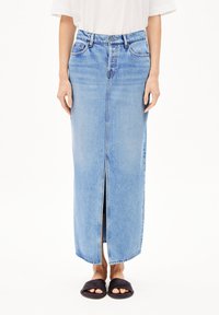 Lichtblauwe denim maxi rok met een voorkniple, hoge taille en riemlussen. Draagt met zwarte slide sandalen. Soepele textuur en klassiek ontwerp.