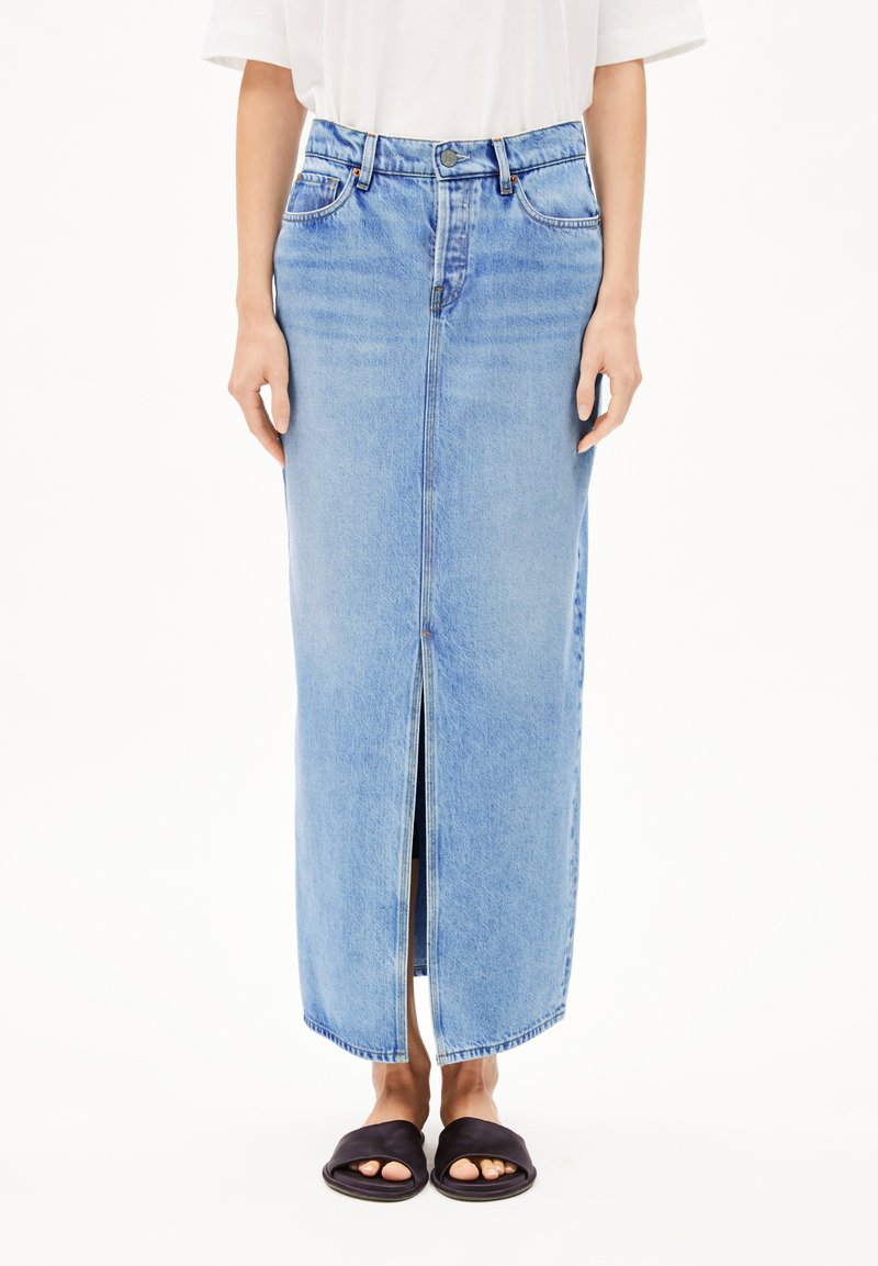 Lichtblauwe denim maxi rok met een voorkniple, hoge taille en riemlussen. Draagt met zwarte slide sandalen. Soepele textuur en klassiek ontwerp.