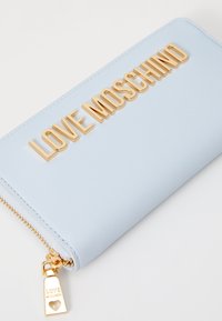 Svetlo modra torbica na zadrgo iz gladkega umetnega usnja. Ima zlato napis "LOVE MOSCHINO" in zlato zadrgo z detajlom srca.