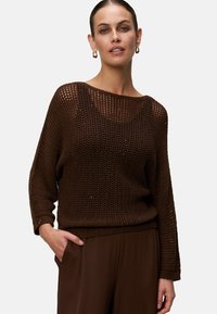 Bruine gebreide trui met een losvallend ontwerp, brede halslijn en een gestructureerde open geweven stof. Gecombineerd met bijpassende bruine broek.