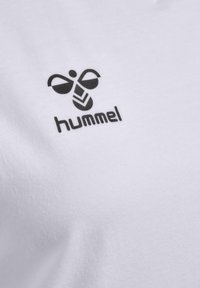 Hvid bomulds T-shirt med et sort Hummel-logo med et stiliseret bi-design og tekst, placeret øverst til venstre på stoffet.