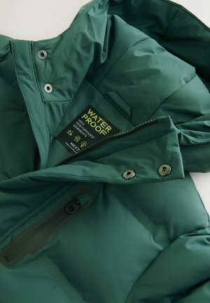 Interno di una giacca impermeabile verde, con una texture liscia, tasca con zip e etichetta con logo e istruzioni per la cura.