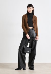 Gilet en tricot brun avec un col roulé noir, associé à un pantalon en cuir noir ample et un petit sac à main noir, doté de quincaillerie en argent.