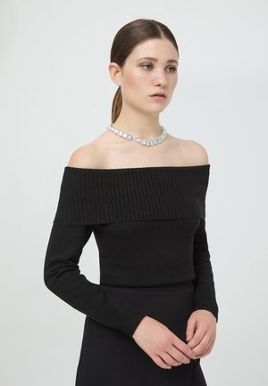 Top nero in maglia off-the-shoulder con scollatura a coste, maniche lunghe e silhouette aderente, abbinato a una collana con gemme trasparenti scintillanti.
