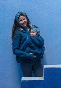 Felpa con cappuccio di un colore teal uniforme, dotata di una tasca con zip per trasportare un bambino. Fasce per capelli coordinate sia per l'adulto che per il bambino.