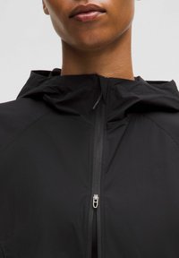 Sort letvægtsjakke med hætte, fuld lynlås, glat tekstur og minimalistisk design med vinkelformede sømdetaljer.