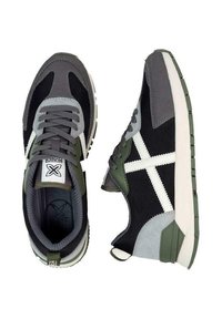 Zapatillas deportivas negras y grises con acentos en verde, que cuentan con materiales de malla y ante, rayas blancas a los lados y una suela texturizada.