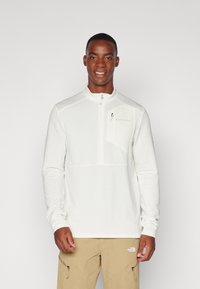 Pull-over blanc à manches longues en matériau texturé avec un col zippé à mi-hauteur. Comprend une petite poche sur la poitrine et un logo sur le côté gauche.
