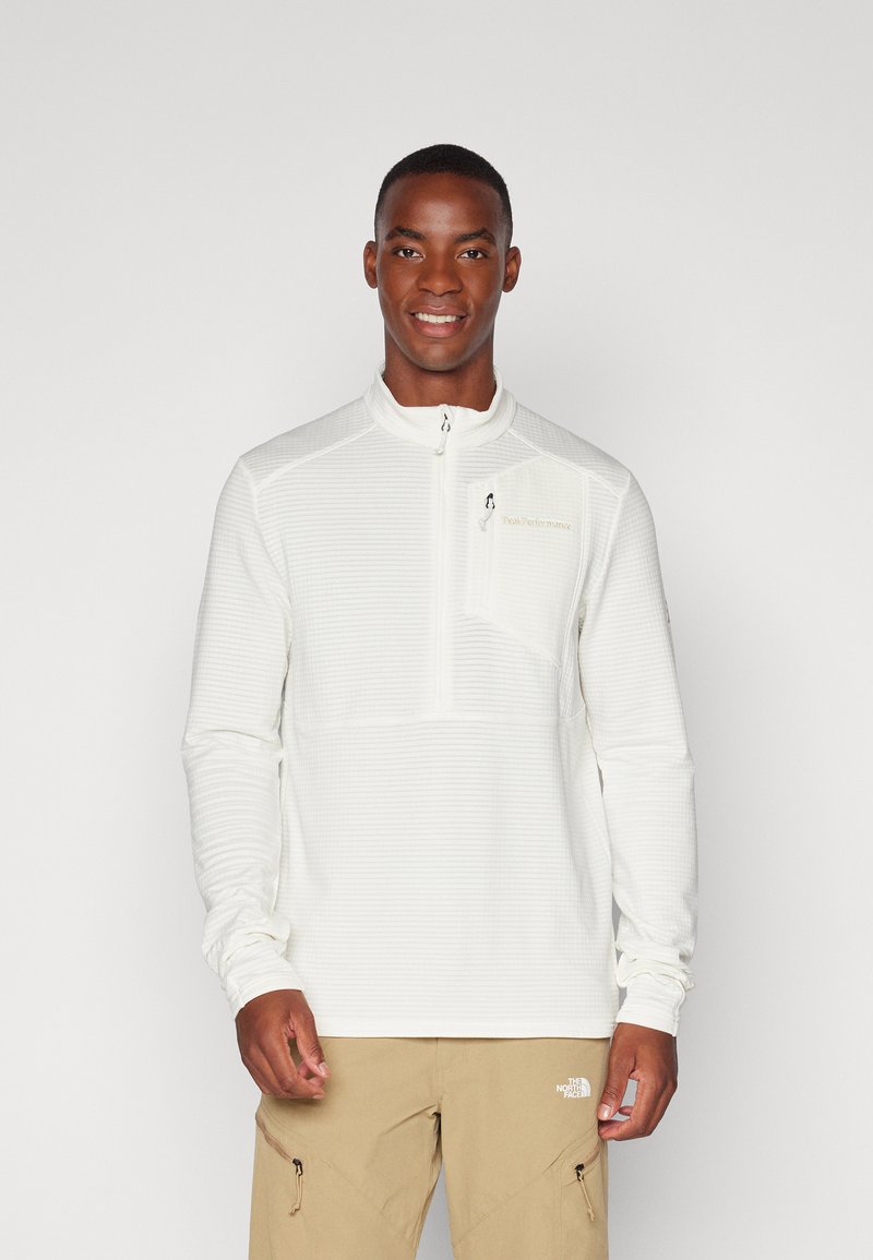 Pull-over blanc à manches longues en matériau texturé avec un col zippé à mi-hauteur. Comprend une petite poche sur la poitrine et un logo sur le côté gauche.