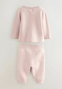 Ružový bavlnený sveter a zodpovedajúci set nohavíc. Sveter má tri gombíky na krku; nohavice majú ribbované manžety a biely vzor.