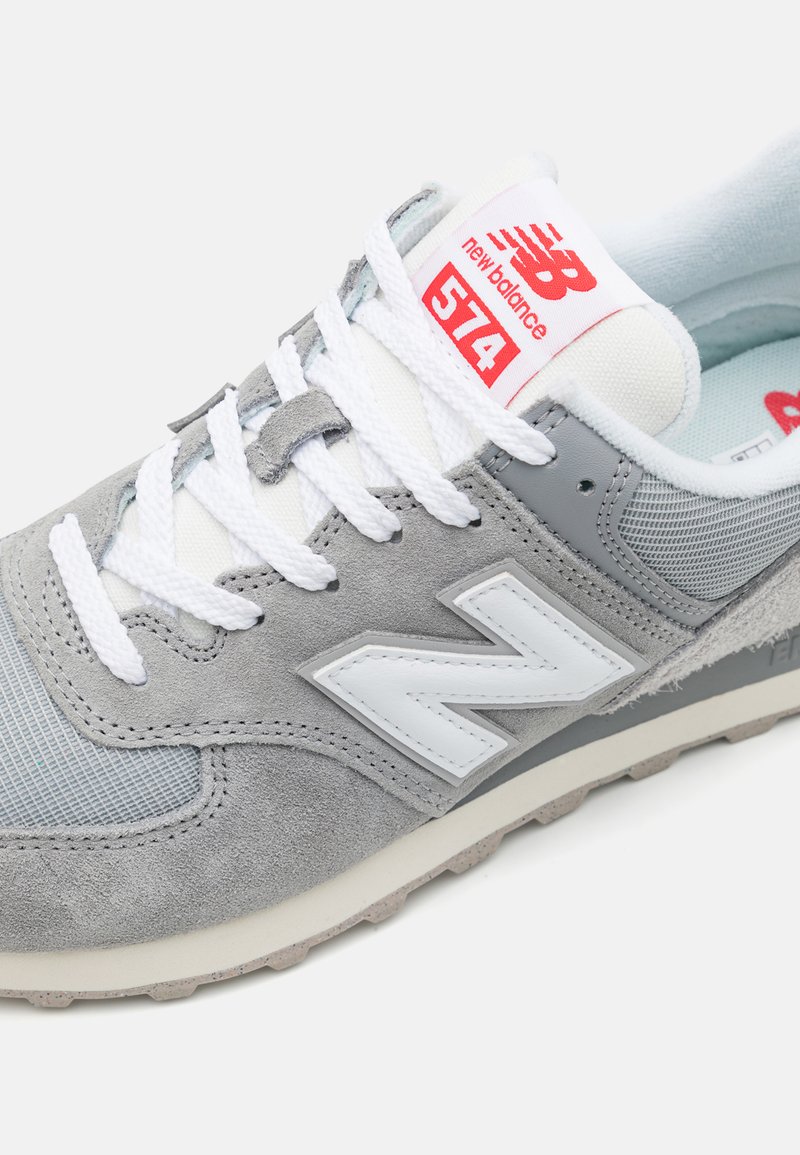 Baskets en suède gris et en mesh avec des accents blancs. Comprend des lacets blancs, une languette rembourrée avec une étiquette rouge et une semelle en caoutchouc texturée.