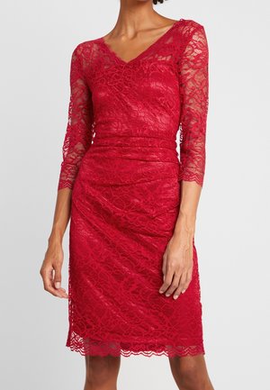 Rotes Spitzenkleid knielang mit dreiviertel Ärmeln, V-Ausschnitt und tailliert an einer schlanken Person vor neutralem Hintergrund.