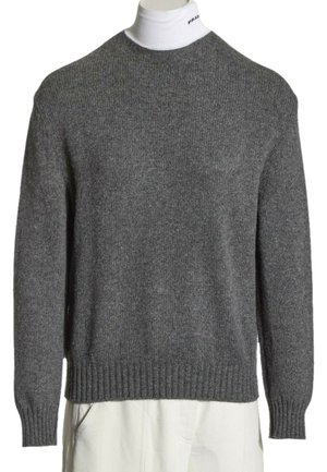 Pull en maille gris porté sur un col roulé blanc avec un petit texte noir sur le col, associé à un pantalon blanc.