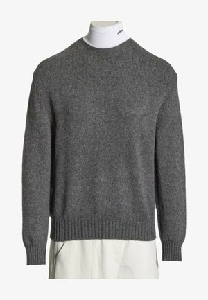 Jersey de punto gris llevado sobre un cuello alto blanco con un pequeño texto negro en el cuello, combinado con pantalones blancos.
