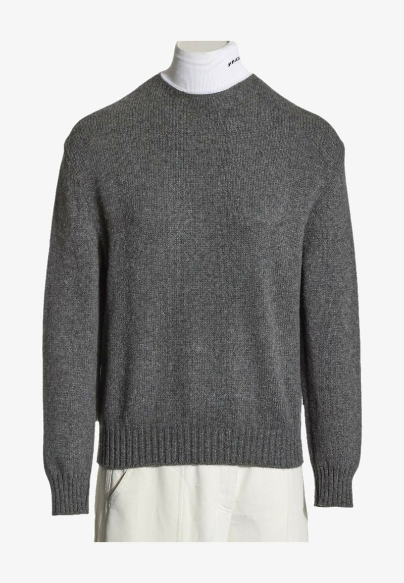 Pull en maille gris porté sur un col roulé blanc avec un petit texte noir sur le col, associé à un pantalon blanc.