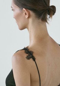 Donna con capelli raccolti in uno chignon vista da dietro, che indossa un vestito nero con delicati dettagli in pizzo sulla sottile spallina.