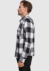 Zwart-wit geblokte flanellen overhemd met lange mouwen, twee borstzakken aan de voorkant en een button-down kraag. Getoond op een mannelijke model in profiel.