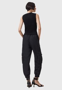 Zwarte geribbelde mouwloze top gecombineerd met zwarte tapse cargo broek met zijzakken en elastische boorden, gedragen met zwarte haksandalen.