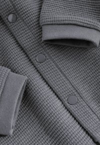 Close-up of gray waffle-knit fabric with snap buttons and ribbed cuffs on sleeves.