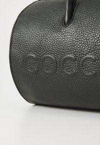 Black textured leather bag with a rounded shape, featuring embossed logo detail. Includes two handles at the top for carrying.