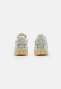 Hvide lædersneakers med ribbede accenter, flade beige gummisåler og kontrastdetaljer ved hælen. Enkel design med minimal branding.