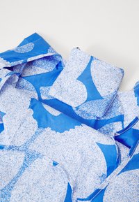 A blue fabric garment featuring large white floral patterns with a speckled texture, draped and partially folded, highlighting design detail.