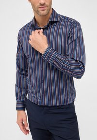 Camicia a maniche lunghe con bottoni, caratterizzata da strisce verticali alternate in blu navy, rosso e azzurro chiaro. Tessuto in misto cotone con colletto classico.