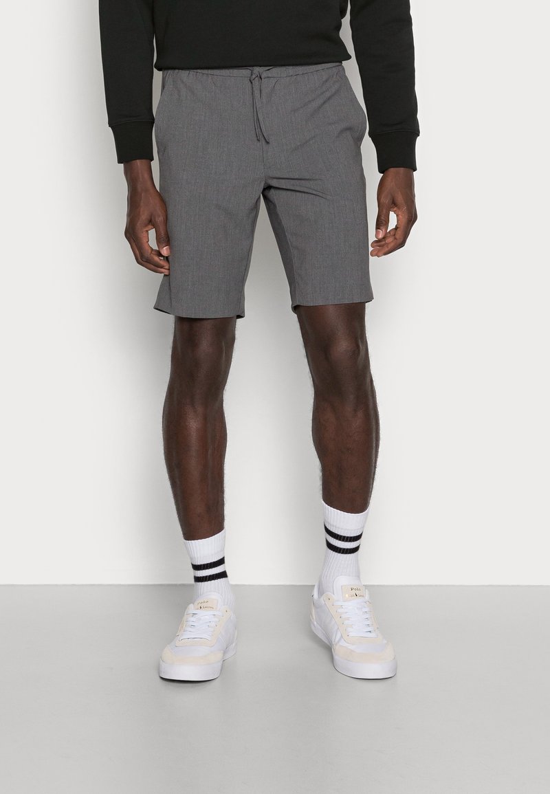 Shorts gris avec une taille élastique et un cordon de serrage. Associés à des baskets blanches et des chaussettes à rayures. Design simple et fonctionnel.