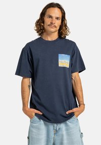 Námořnická modrá bavlněná tričko s krátkým rukávem. Má přední kapsu s modrožlutou grafikou, volný střih a kulatý výstřih.