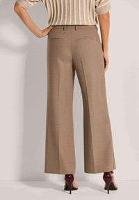 Beige hoge taille wijde broek met een gladde textuur, voorzien van twee achterzakken en een kreukeldetail, gecombineerd met bordeauxrode hakken.