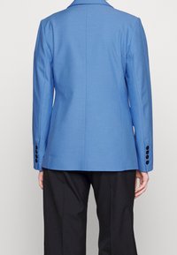Dopasowana niebieska marynarka z gładkiego materiału z klasycznymi klapami, posiadająca sześć czarnych guzików na rękawach oraz prosty fason z tyłu.