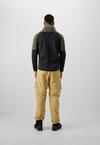 Veste à capuche en polaire navy et olive, associée à un pantalon cargo beige. Des chaussures noires complètent la tenue.