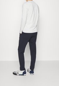 Lichtgrijze langemouwen shirt, marineblauwe broek en grijs/marineblauwe sneakers. Gladde stof, comfortabele pasvorm en strakke lijnen met een minimalistisch ontwerp.