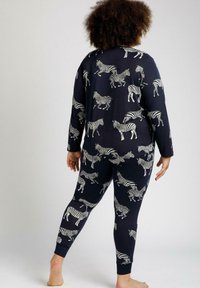 Conjunto de pijama navy que incluye una camiseta de manga larga y pantalones ajustados. Ambos están decorados con patrones de cebras blancas en toda su superficie y están confeccionados con una tela suave.