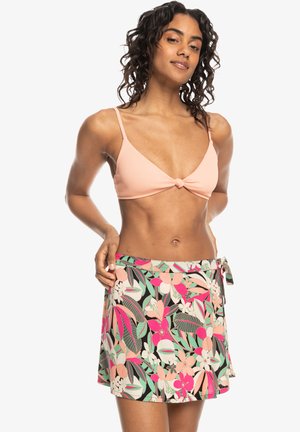Top de bikini de color rosa con detalles anudados; falda envolvente de estampado floral multicolor con lazo en el lado, que presenta hojas verdes y flores brillantes.