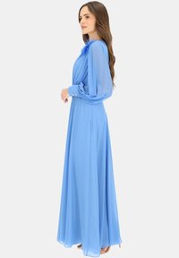 Sukienka z długim rękawem, w jasnoniebieskim kolorze, o płynnej sylwetce, z plisowanym przodem i piórowymi akcentami na ramieniu. Gładki, lekki materiał.