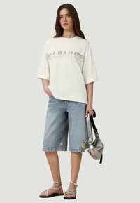 White oversized t-shirt with a gray graphic print, paired with distressed light blue denim bermuda shorts and shiny silver accessories.
