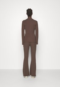 Brun ribbad stickad topp och vida byxor, med figursydd design, långa ärmar och subtil textur, sedd bakifrån.