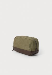 Green canvas toiletry bag with a brown faux leather base, rectangular shape, zip closure, and side pull tab for easy handling.