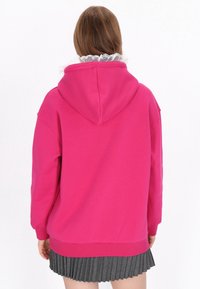 Forró rózsaszín kapucnis pulóver húzózsinóros kapucnival és bordázott mandzsettával. Alulról kilátszó fodros fehér gallérral díszítve. Egyszerű, sima hátoldalú.