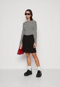 Sort med knapp ned i denim kombineres med en langermet topp med svart og hvitstripe. Tilbehøret inkluderer en rød veske og svarte klumpete sko.