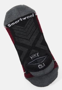 Calcetín negro y rojo con un puño gris, que presenta un diseño en chevron y el nombre de la marca "Smartwool" cerca de la parte superior. Información de talla incluida.