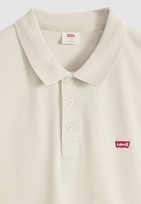Polo beige Levi's avec trois boutons, col classique et petit logo rouge Levi's sur la poitrine gauche.