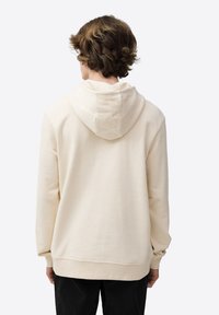 Sudadera beige hecha de tela suave, con capucha forrada, puños elásticos y un corte relajado. Textura lisa sin patrones visibles.