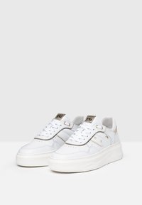 White sneakers with a textured leather upper, featuring metallic accents, lace-up design, platform sole, and geometric stitching details.